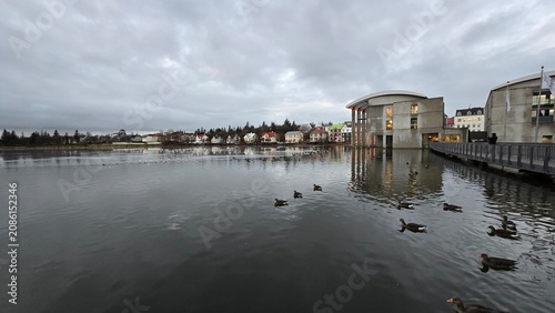 Foto Tjörnin lake and Reykjavik City Hall under a cloudy sky.