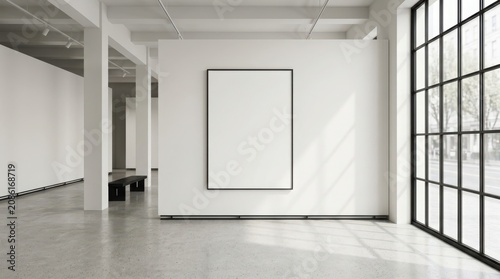 Empty vertical picture frame hanging on a clean wall in a bright modern art gallery room with large windows and sunlight