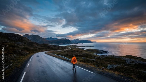 A lone traveler walking on a scenic coastal road in Norway at sunset.
