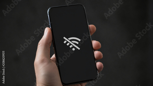 A hand holds a smartphone displaying a no Wi-Fi connection icon on the screen against a dark background.
