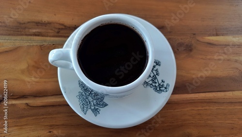 Cup of Black Coffee on Saucer with Floral Pattern on Wooden Table. Business Background