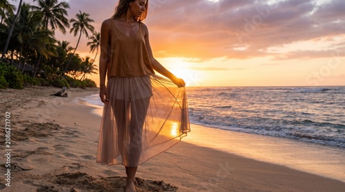Sensual young woman holding sheer skirt while walking on sandy beach at sunset