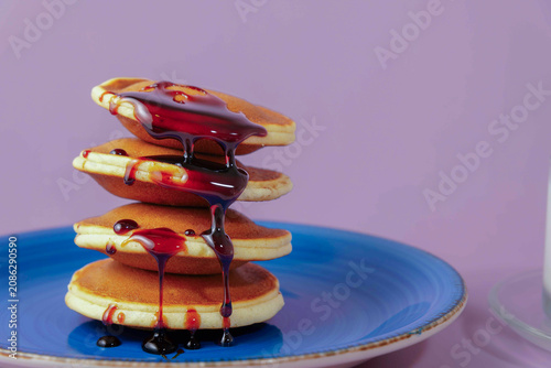 Stack of fluffy pancakes topped with flowing berry syrup on a blue plate, set against a vibrant purple background
