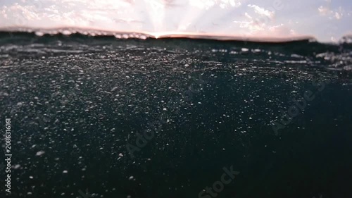 Underwater part and sunset skylight splitted by waterline, underwater bubbles. Beautiful clouds and bright sun over sea water, Real image very suitable for backgrounds in Mediterranean sea, undersea.