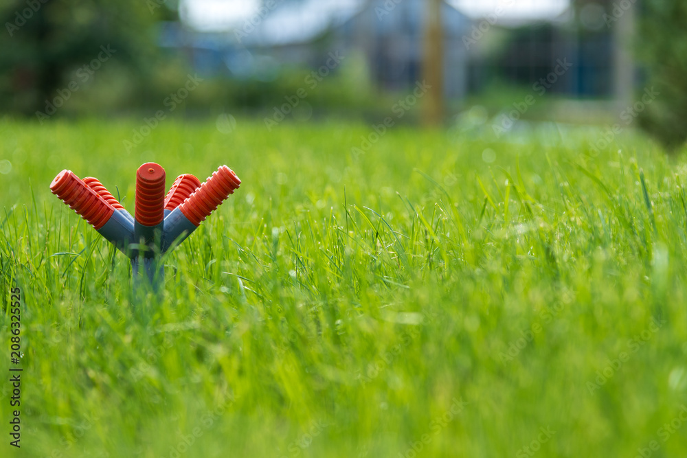 © ZeDesign - Garden sprinkler on green grass with copy space for text. A plastic lawn irrigation sprinkler placed on the left side of the frame on a vibrant green grass field, creating a large empty space