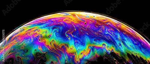 Vibrant iridescent soap bubble surface featuring swirling patterns of liquid color against a deep black background for abstract artistic backgrounds