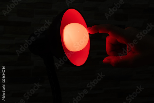 Hand Turning On Small Desk Lamp With Warm Red Light