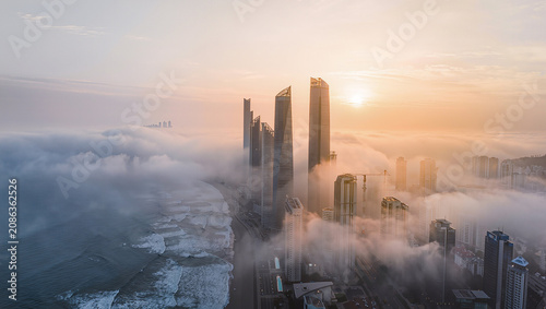 Aerial view of city skyscrapers emerging from morning fog at sunrise.