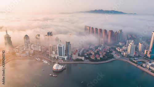City skyline enveloped in fog at sunrise over calm sea waterfront