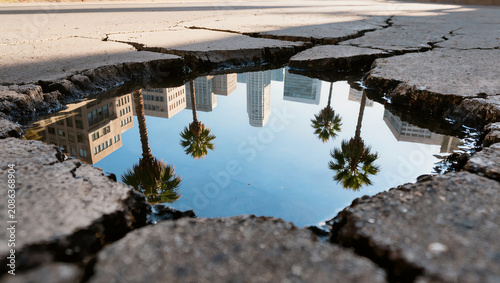 Cityscape reflection in cracked asphalt puddle, palm trees, urban landscape