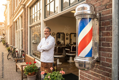 Barber standing proudly outside vintage barbershop with pole  