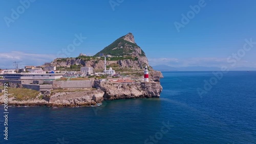 Drone footage rising and panning over Europa Point — Rock peak, mosque minaret, lighthouse, power station, limestone cliffs, and Morocco faintly visible across the Strait.
