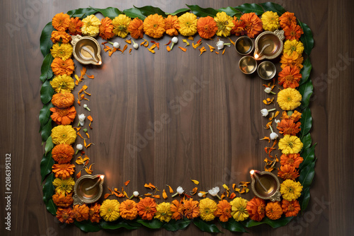 Diwali festival floral frame with marigold flowers and oil lamps. Traditional Indian celebration border on wood background. Decorative rangoli with diya.