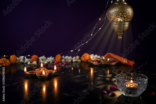 Traditional Diwali celebration with glowing diya oil lamps, golden lantern with light rays, festive flower garland on dark marble surface