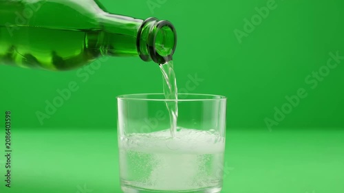 Green liquid pouring into glass with effervescent bubbles forming during process in studio lighting