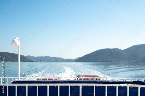 View of a ship's wake and a distant bridge from the deck