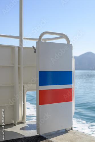 Minimalist close-up of a safety gate with blue and red stripes on a ferry deck