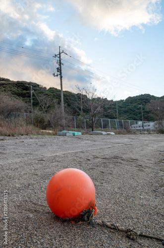 A solitary orange fishing buoy resting on a gravel beach