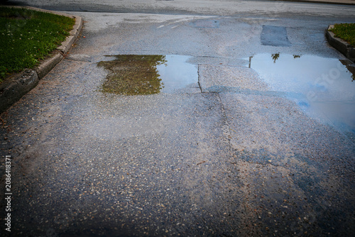 Fotografía A wet asphalt road with shallow puddles of rainwater reflecting the sky, trees, and roadside curbs