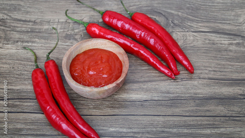 Fotografía Chilli sauce and fresh peppers on wooden background