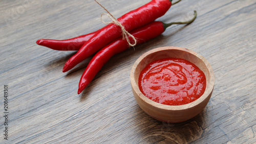 Photos Chilli sauce and fresh peppers on wooden background