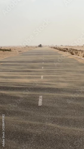 Road through a desert landscape. Empty desert road with strong wind blowing sand over the asphalt.