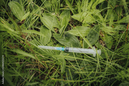 Fotografie A used syringe lying in long, green grass illustrates the pollution of medical waste, public health risks, and improper disposal in the natural environment