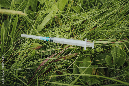 Фотография A used syringe lying in long, green grass illustrates the pollution of medical waste, public health risks, and improper disposal in the natural environment