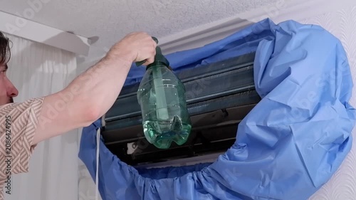 Male technician cleaning and washing an indoor air conditioner unit with a water sprayer at home