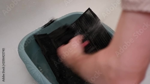 Male hands washing a dirty air conditioner filter with running water in a bathtub
