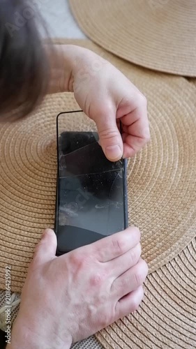 Male hands carefully peeling off a cracked tempered glass screen protector from a mobile phone