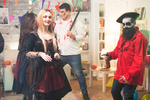Fotografía Shy blond woman dressed as a vampire poses during a Halloween party, showing costume makeup and festive character style, adding festive character styling, dress-up atmosphere and seasonal party mood