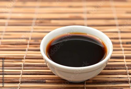 Close-up of soy sauce in white bowl on bamboo mat