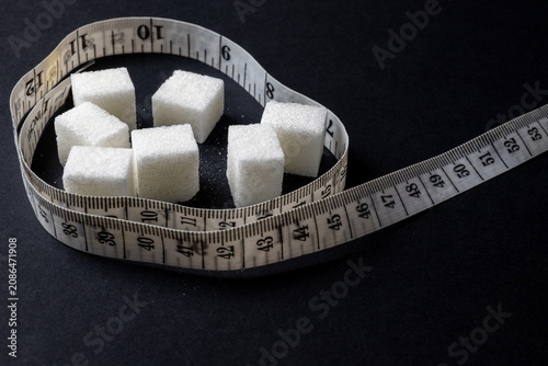 Sugar cubes and measuring tape on black background representing diet concept