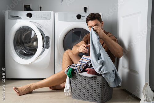 Canvastavla Happy man sorting clothes near washing machine in laundry room