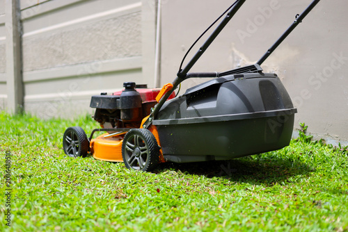 Obraz na płótnie An orange engine-powered lawn mower being used to cut green grass in a backyard garden