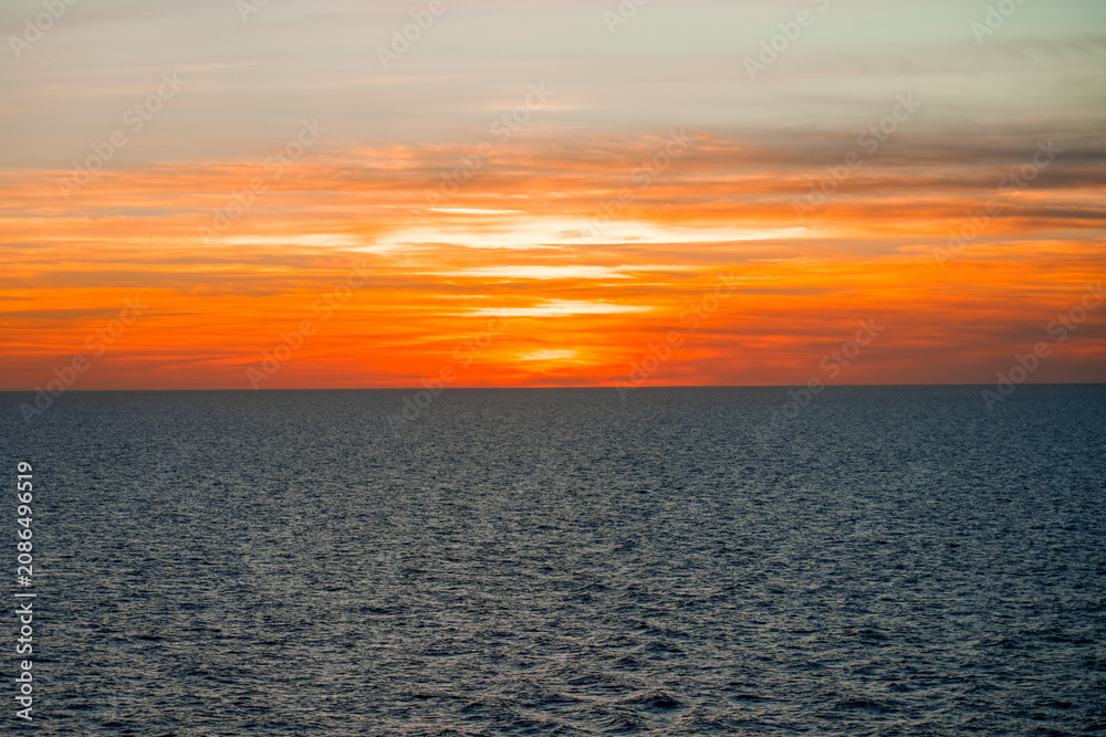 Fototapeta premium Glowing sunset with clouds over the sea. Evening sky in shades of orange. 