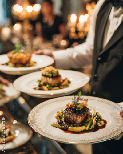 Professional waiter elegantly serving a gourmet main course to guests in a luxury restaurant, beautifully plated food, sophisticated dining room, warm golden lighting