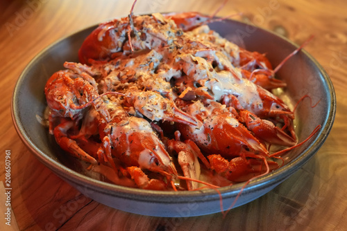 Boiled crayfish served in a bowl with creamy garlic sauce and herbs on a rustic wooden table. Gourmet seafood appetizer, restaurant cuisine, close-up food photography with appetizing presentation.