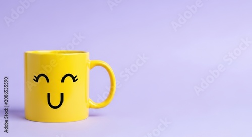 Bright yellow mug with a cheerful smiley face design, isolated on a soft purple background
