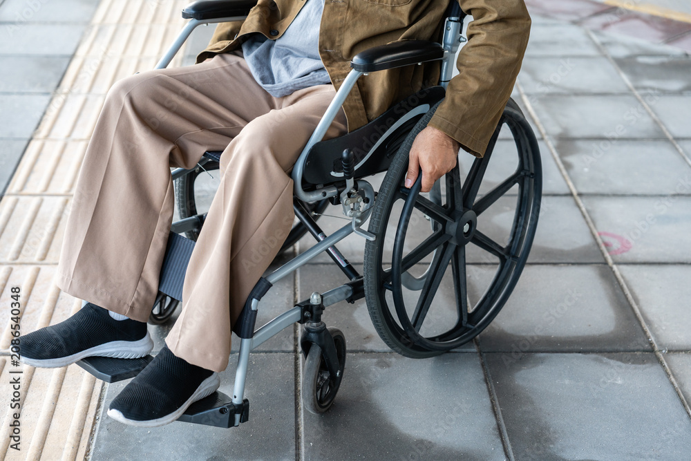 Fototapeta premium A man with a leg disability who cannot walk uses a wheelchair and travels by the train at a station He walks along the sidewalk where there are signs indicating accessibility for disabled individuals