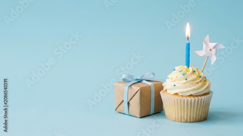 Sweet Birthday Cupcake with Lit Candle and Wrapped Gift Box on Light Blue Background