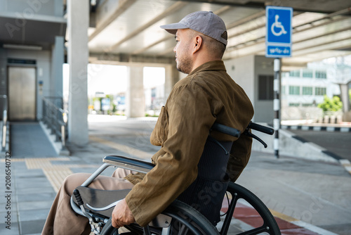 A man with a leg disability who cannot walk uses a wheelchair and travels by the train at a station He walks along the sidewalk where there are signs indicating accessibility for disabled individuals