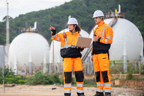 Team of Industrial engineers using laptop and radio to monitor gas storage tank system, Technical team in safety uniform discussing maintenance plan at fuel storage facility