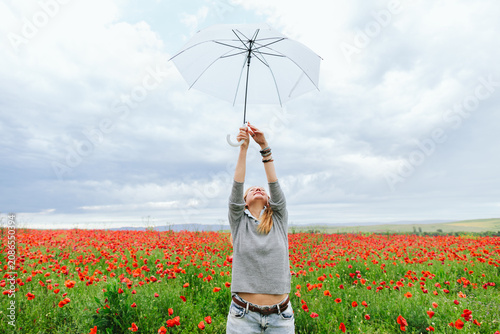 Carefree woman raises a white umbrella in a red poppy field
