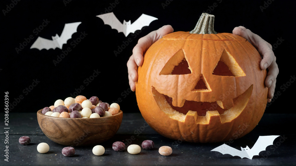 Hands holding a carved Jack-o'-lantern with a bowl of candy for Halloween