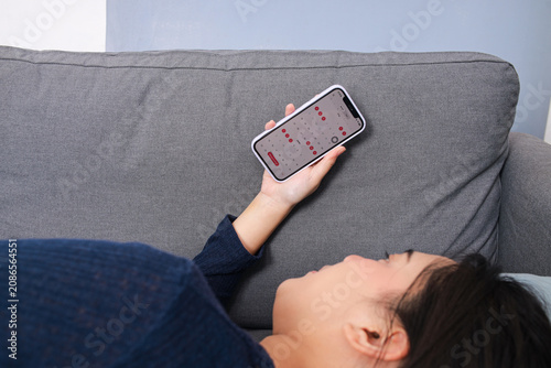Woman Lying On Couch Holds Smartphone To View Calendar App Showing Tracked Dates