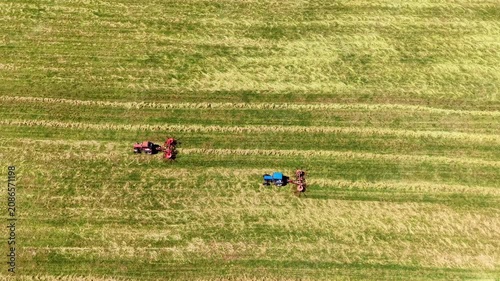 Tractors preparing fields with parallel lines of freshly cut grass in the summer sun, aerial view