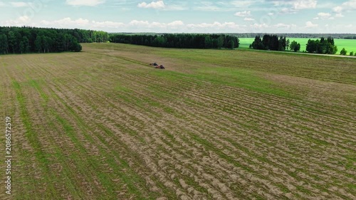 Tractors cutting grass in expansive green field during clear sunny day with few clouds, aerial view