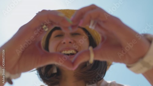 A happy young woman on the beach forms a heart shape with her hands, standing against the backdrop of the sea. a romantic mood.
